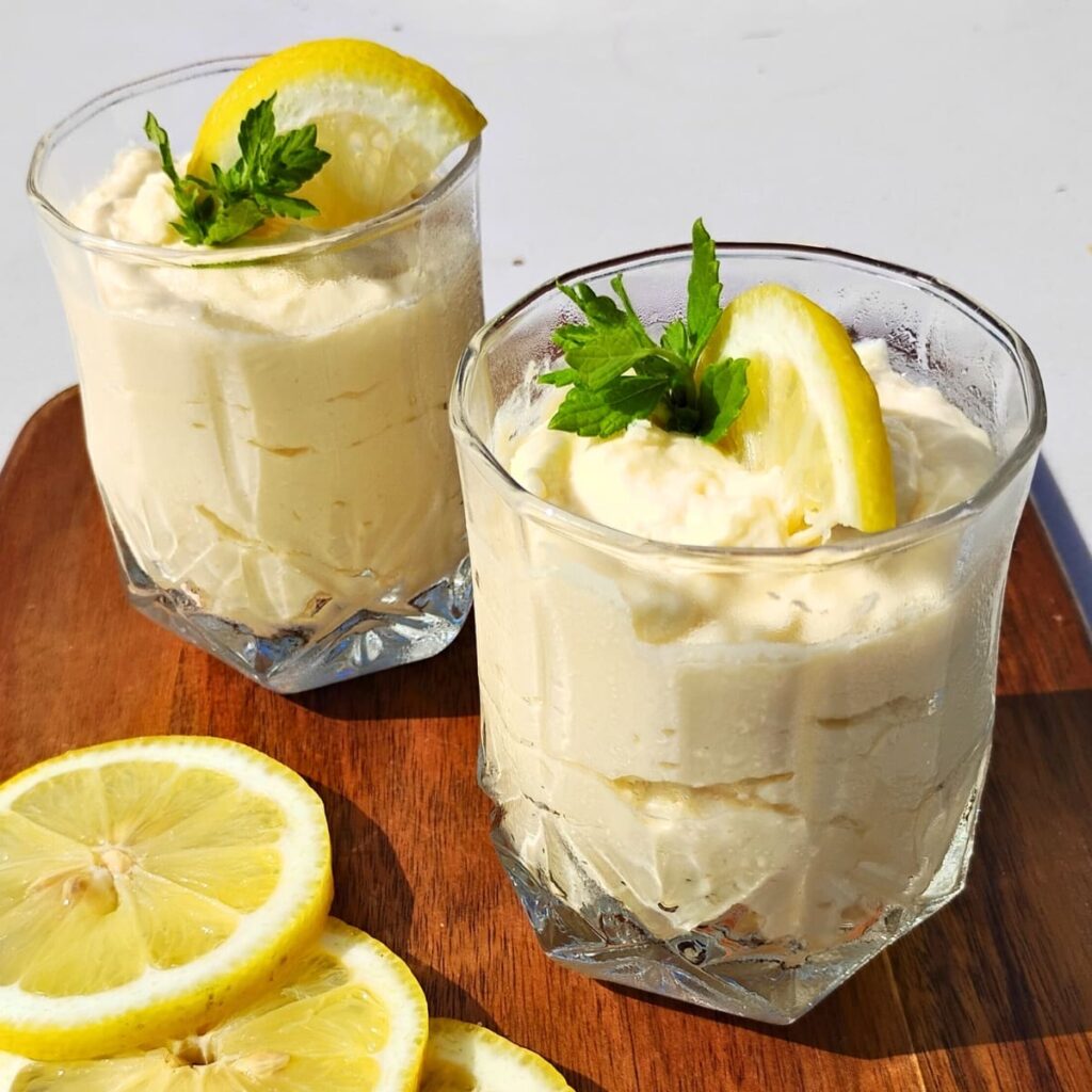 photo shows two glasses filled with lemon cheesecake mousse and decorated with lemon slices and sprigs of lemon balm.