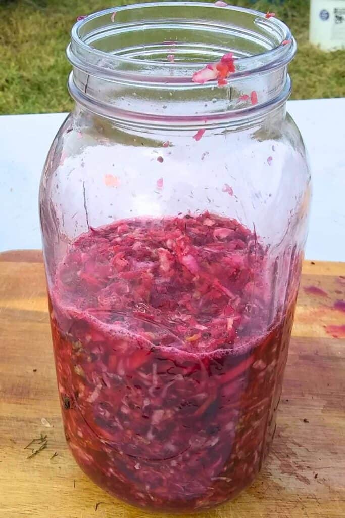 a jar is half full with fermented coleslaw ingredients and natural vegetable juices.