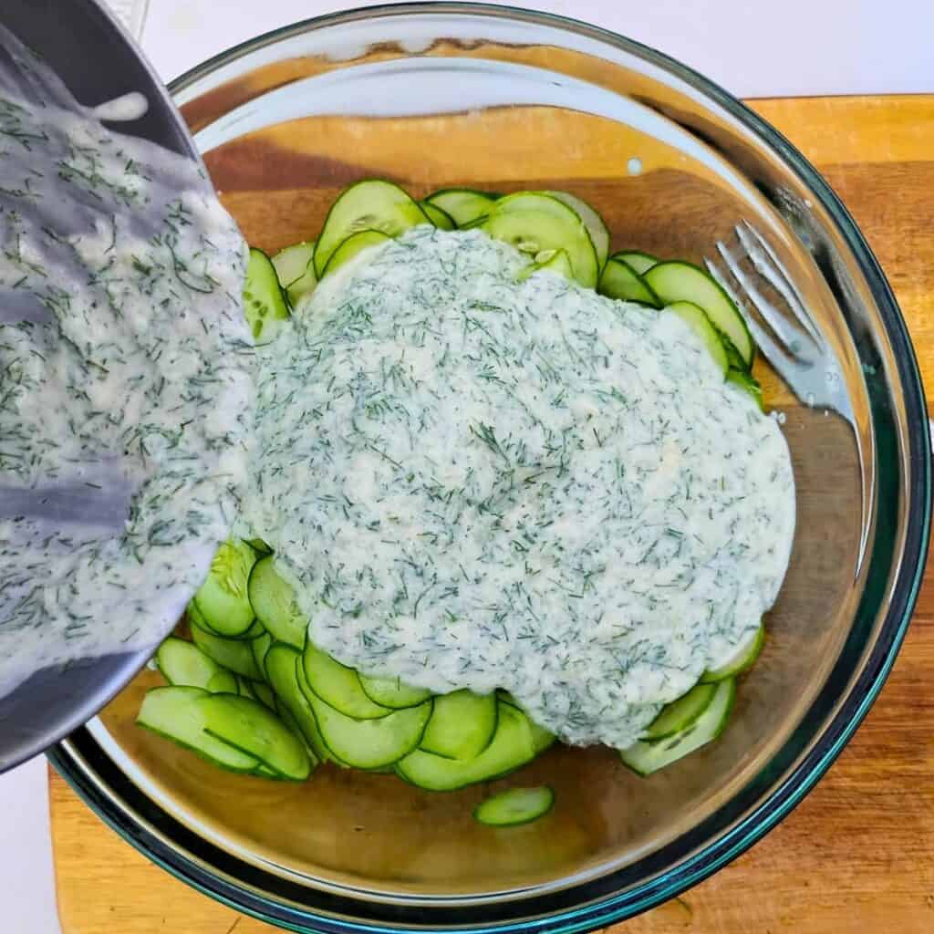 Salad dressing is getting poured over cucumber slices in a bowl.