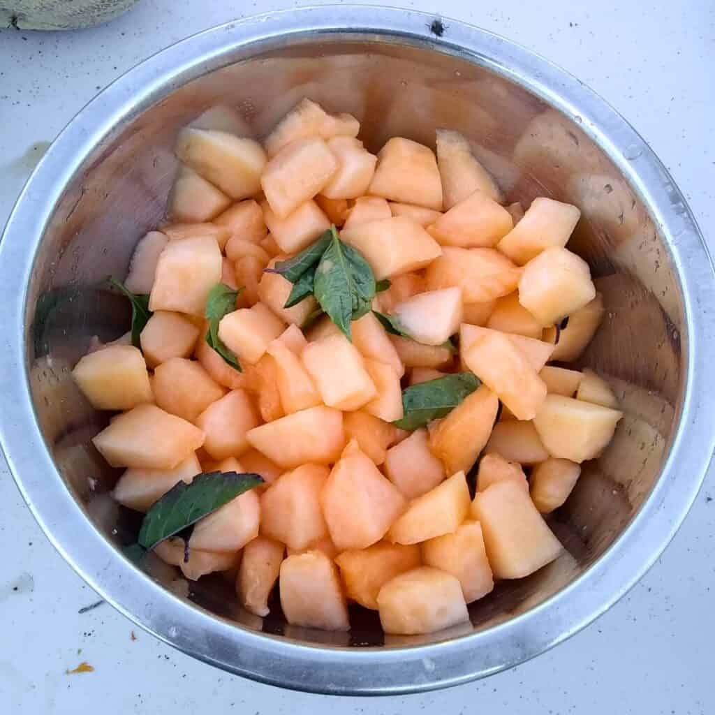 a bowl full of cantaloupe pieces with basil. 