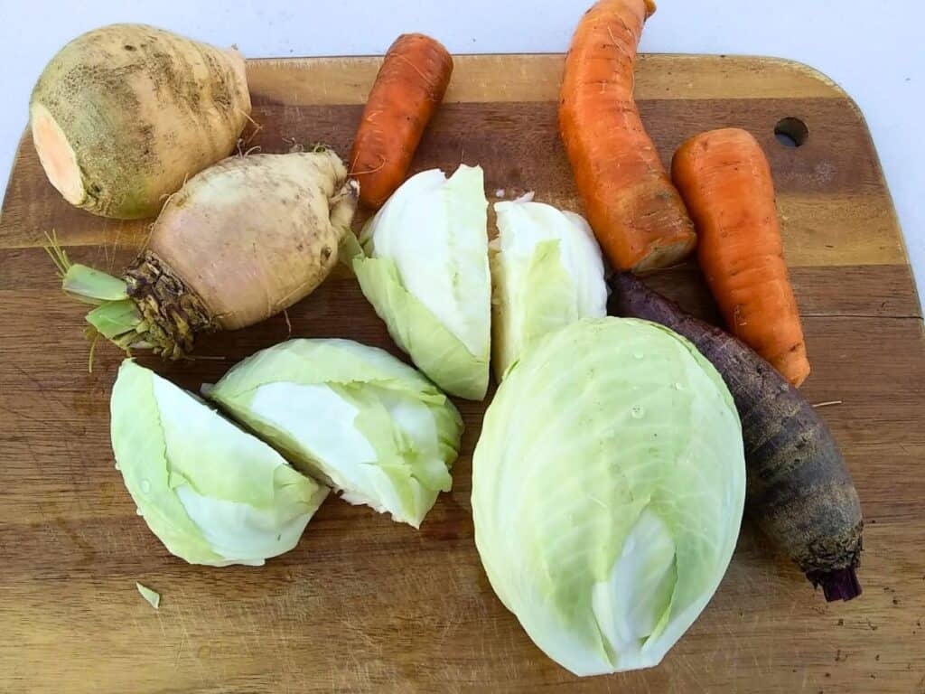 a cutting board with a medley of root vegetables and a couple of heads of cabbage.
