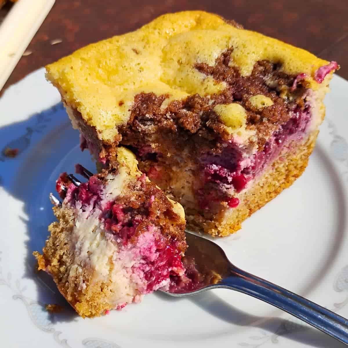 photo shows a piece of blackberry cheesecake streusel bar with a small piece removed by a fork.