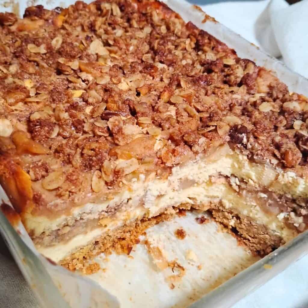 A baking pan with an apple pie cheesecake that has a few slices removed to show texture.