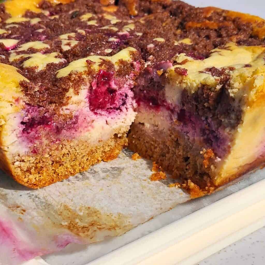 a whole baked blackberry cheesecake with streusel topping and a piece missing to show texture.