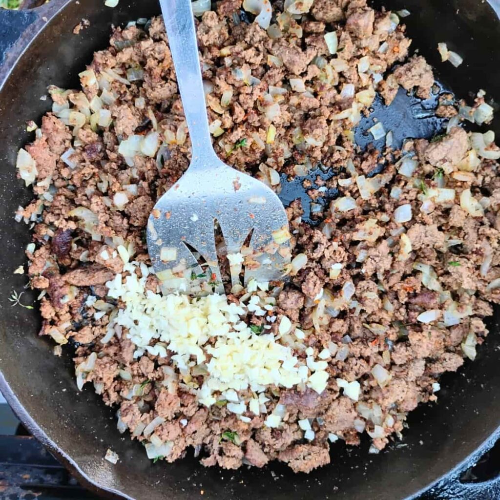 garlic is added to browned beef and onions in a pan.