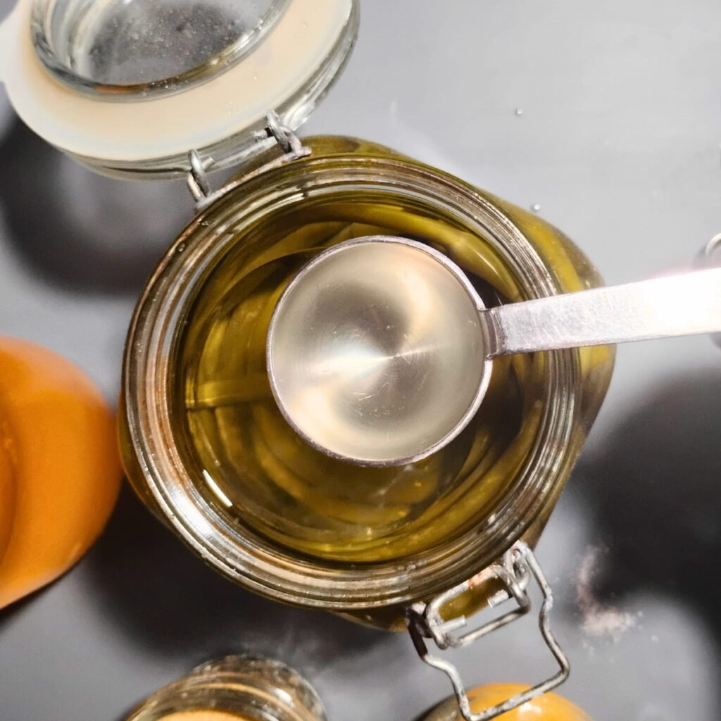 A spoon is scooping some fermentation brine from a jar of fermented garlic scapes.
