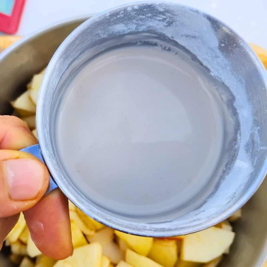 an arrowroot slurry in a measuring cup over a pot with the apple pie filling ingredients.