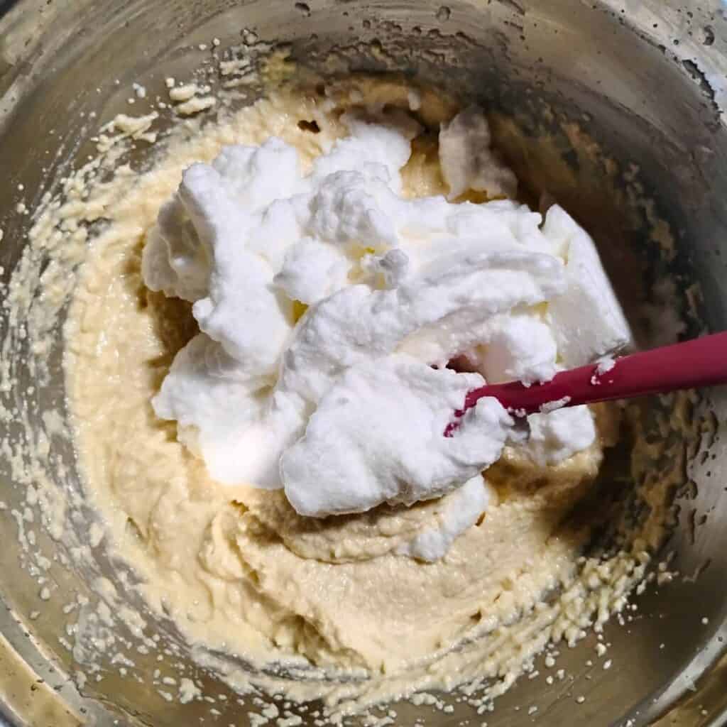 progress photo shows stiff eggwhites have been added to a bowl with creamy cheesecake batter, to be folded in for extra fluffiness.