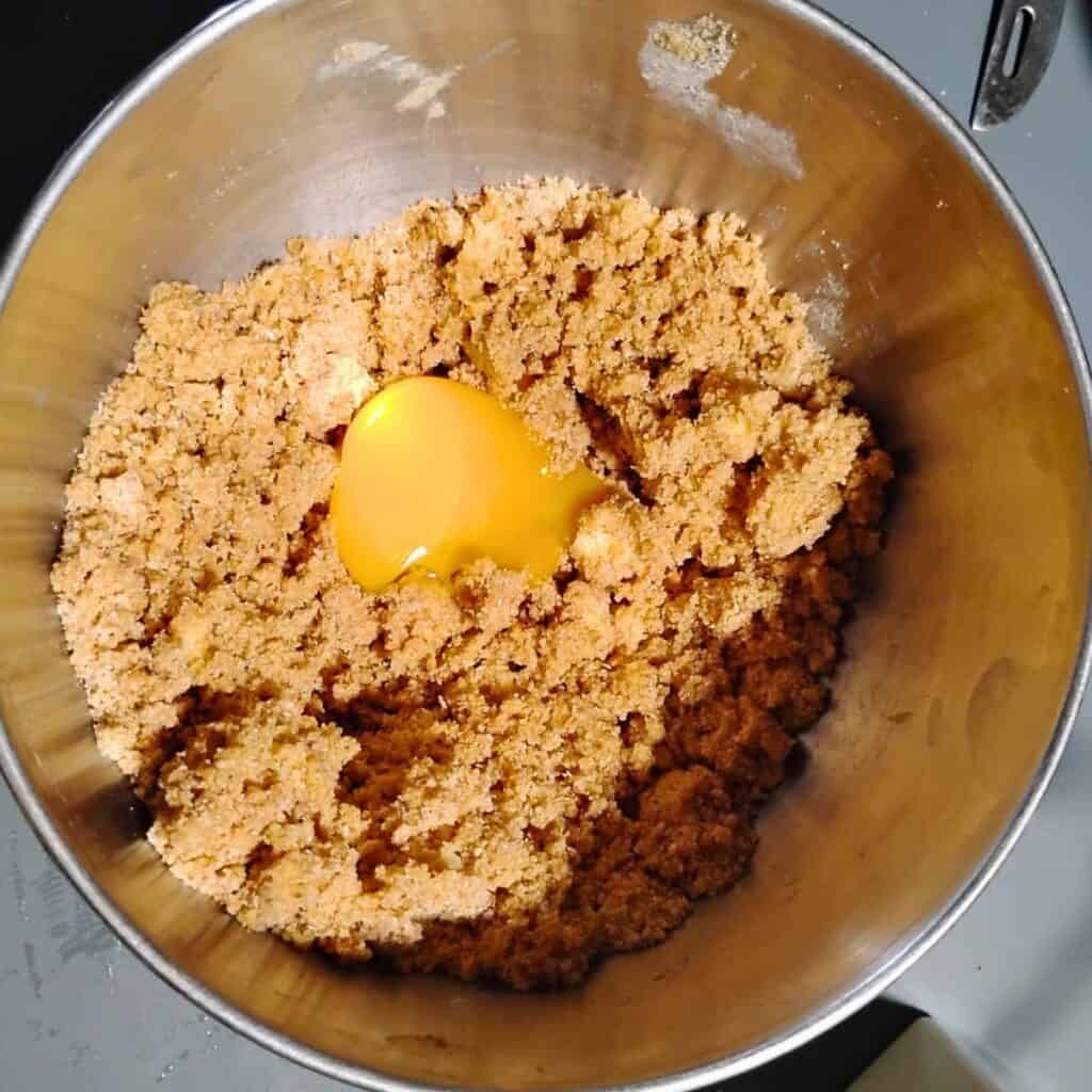 an egg is added to a crumbly mix of pastry crust ingredients.