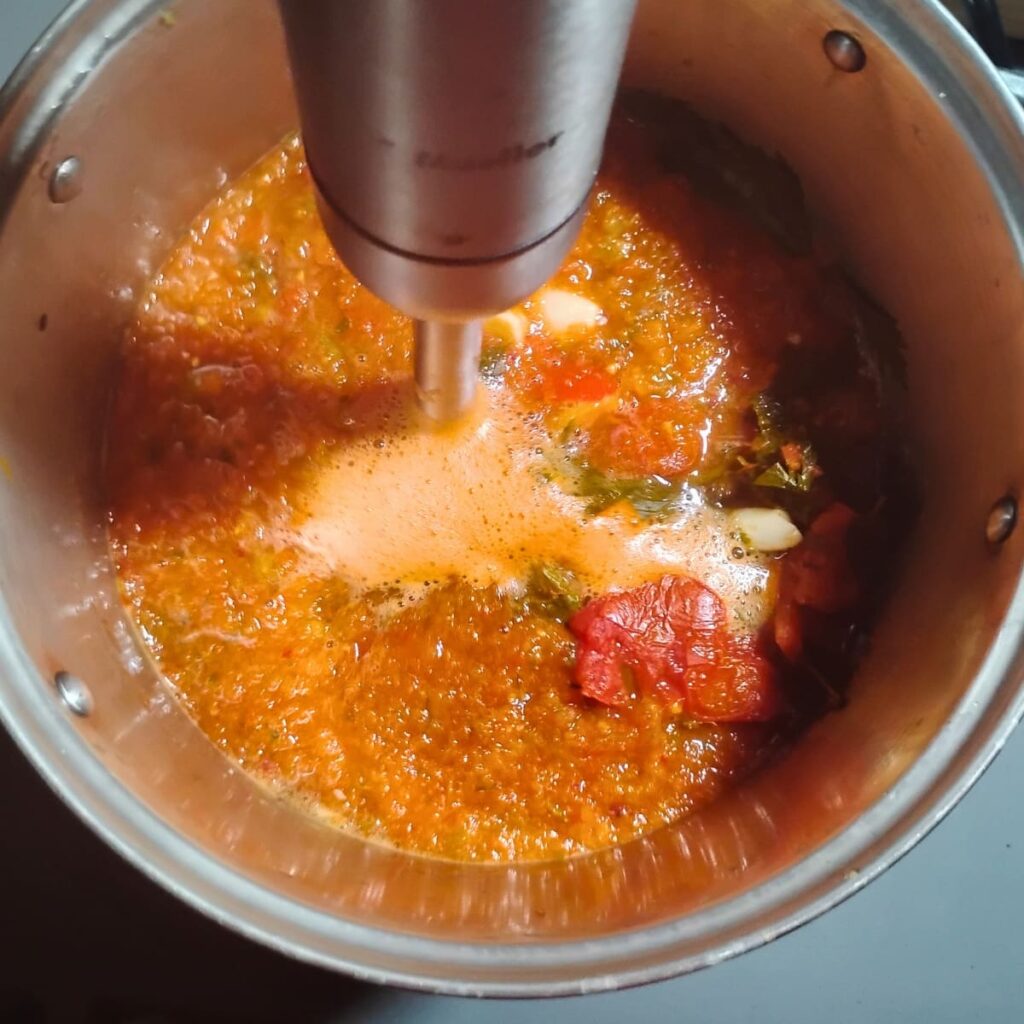 an immersion blender blends vegetables inside a large pot