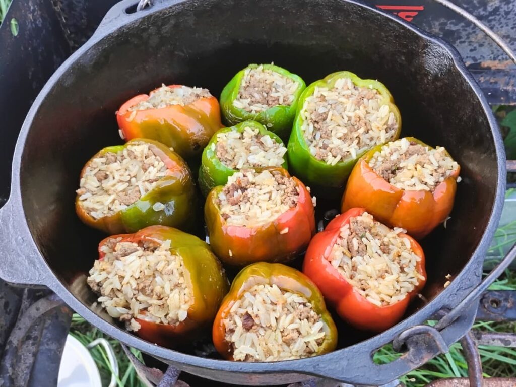 photo shows a cast iron dutch oven filled with rice and beef healthy stuffed peppers on a outdoor propane burner.