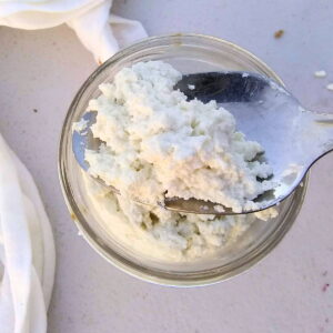homemade ricotta cheese in a jar with a spoon taking some out.
