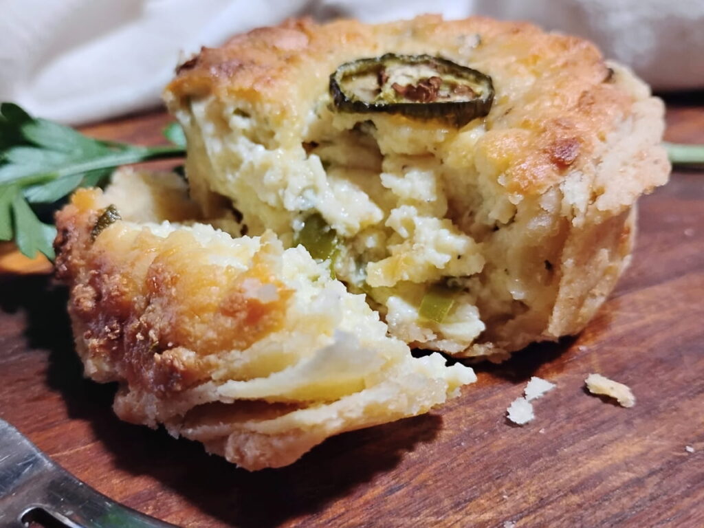 photo of a jalapeno popper pie with a chunk removed and laying on the side, showing off flaky pastry layers and a creamy filling. 