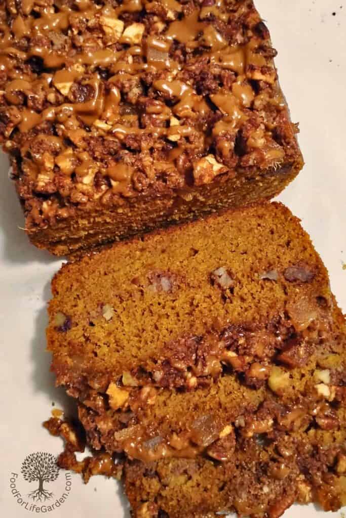 sourdough pumpkin cake with ginger, pecan & apple streusel on a table with maple glaze and with a few slices cut and laying in front.