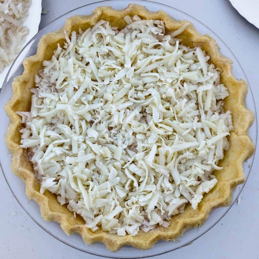 assembly of the pastry lined dish with grated cheese in the bottom.