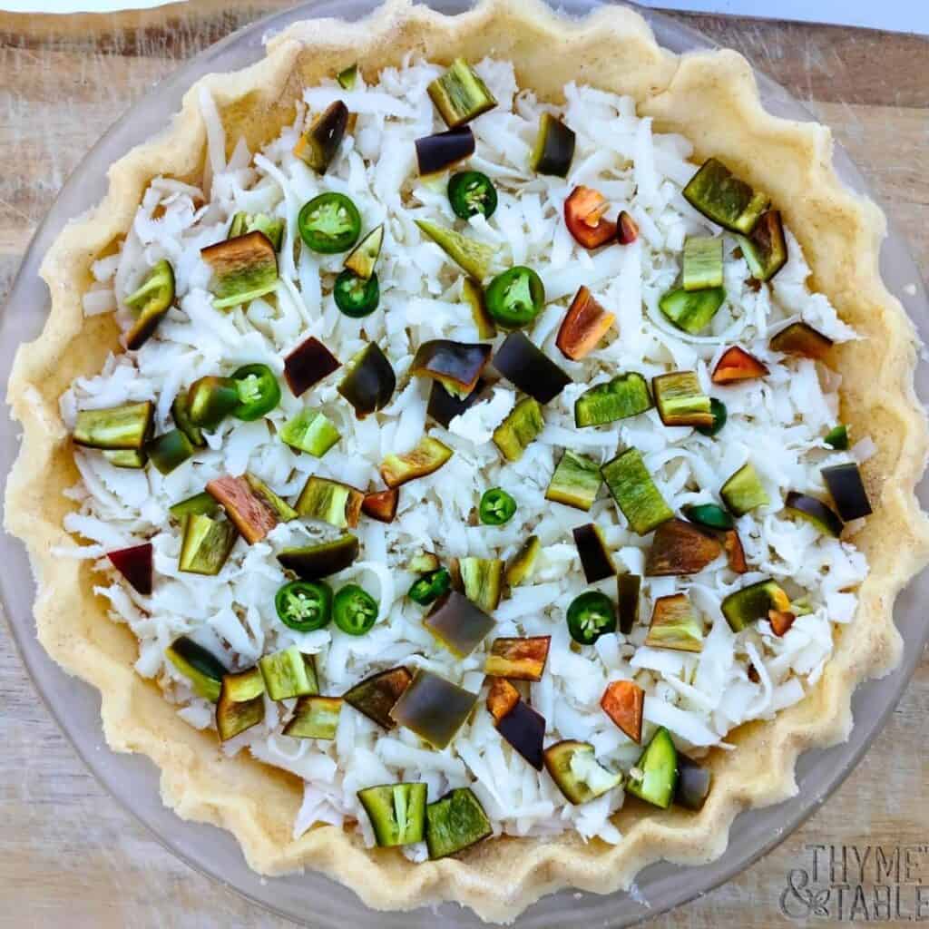 a pie is getting assembled with a crust, filled with shredded cheese and chopped jalapenos.