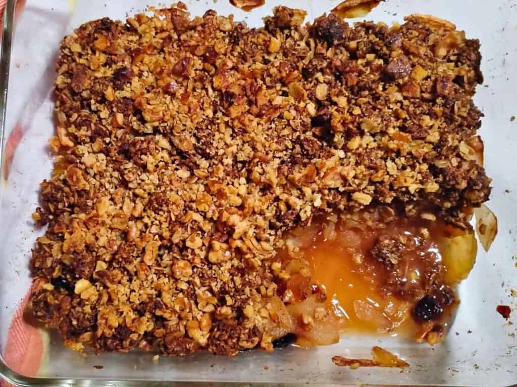a baking dish filled with cranberry apple crisp with a walnut and oatmeal topping. a portion has been scooped out.