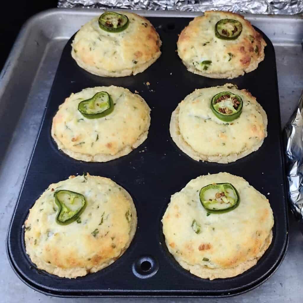 a muffin pan filled with 6 muffin cup sized jalapeno popper quiches in flaky pie crusts, inside a bbq grill.
