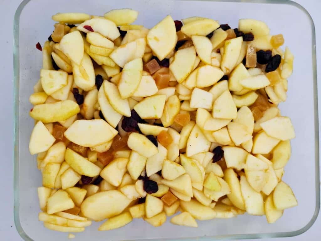 healthy apple crisp ingredients blended inside a baking dish. Apples, cranberries, and diced crystallized ginger.