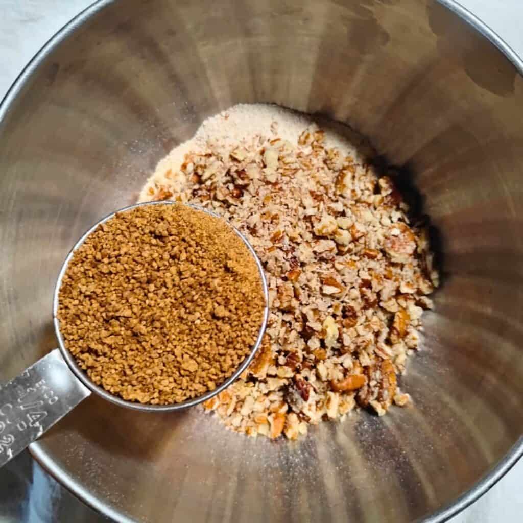panela sugar is added to the pecans and flour in a bowl.