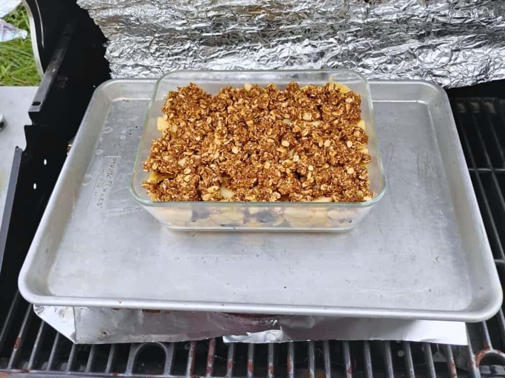 A grill with a baking pan filled with apples, cranberries, ginger, and a buttery walnut crumble topping.