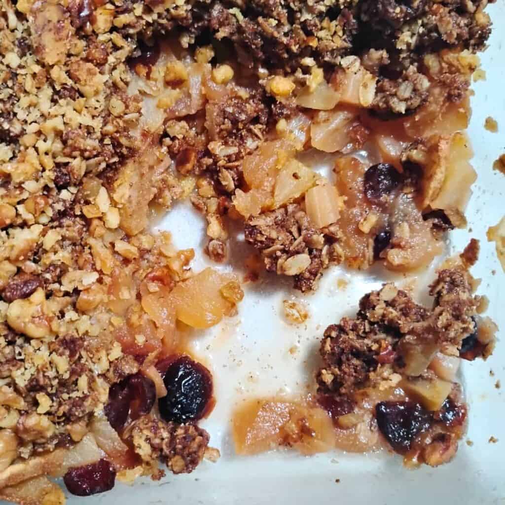 spiced healthy apple crisp with cranberries, diced candied ginger and a walnut crumble topping in a baking dish.