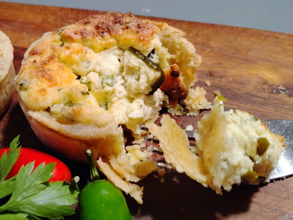 photo of a jalapeno popper quiche cup, fully baked and broken with a fork, showing of the flaky crust and rich filling. 