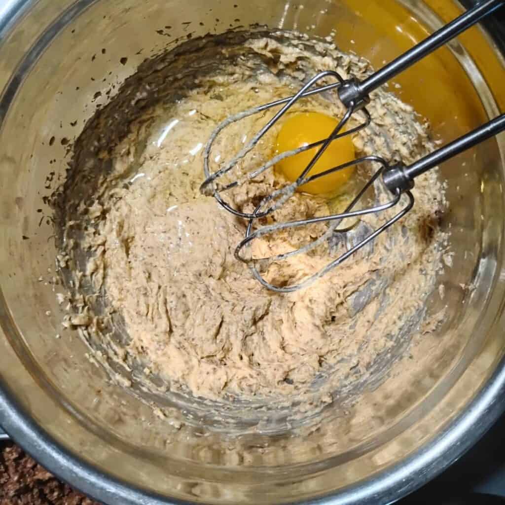 a bowl with creamed butter and sucanat, unrefined cane sugar. an egg has been added and beaters from a hand mixer are showing.