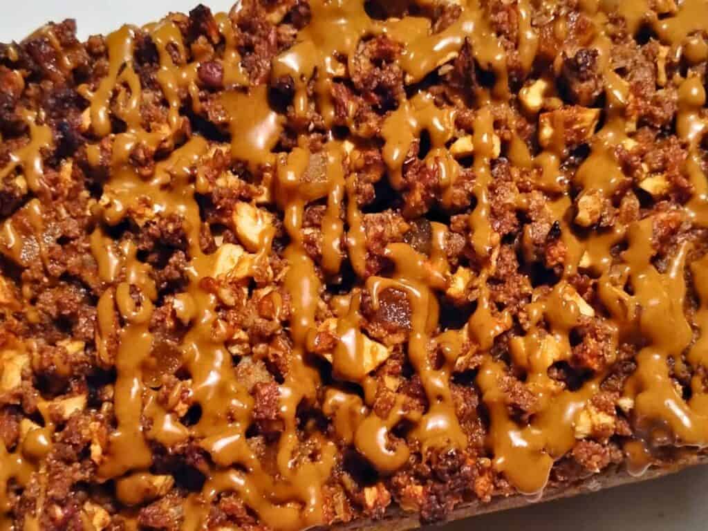 close-up shot of sourdough pumpkin cake with Ginger, pecan & Apple Streusel, showing the topping and a glaze drizzled over the top. 