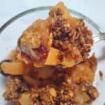 ginger and spice healthy apple crisp with cranberries in a bowl dand a spoon is scooping out some of it.