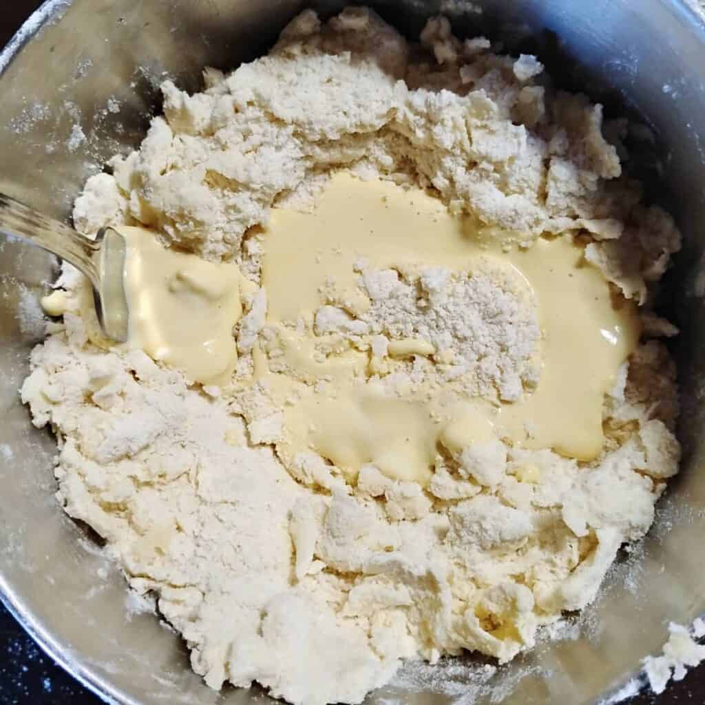 a bowl filled with flaky butter and flour and some wet ingredients poured over the top.