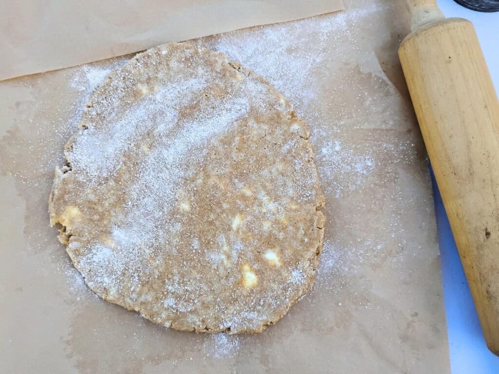 photo shows a pie crust getting rolled out on a piece of parchment paper with a rolling pin next to it. 
