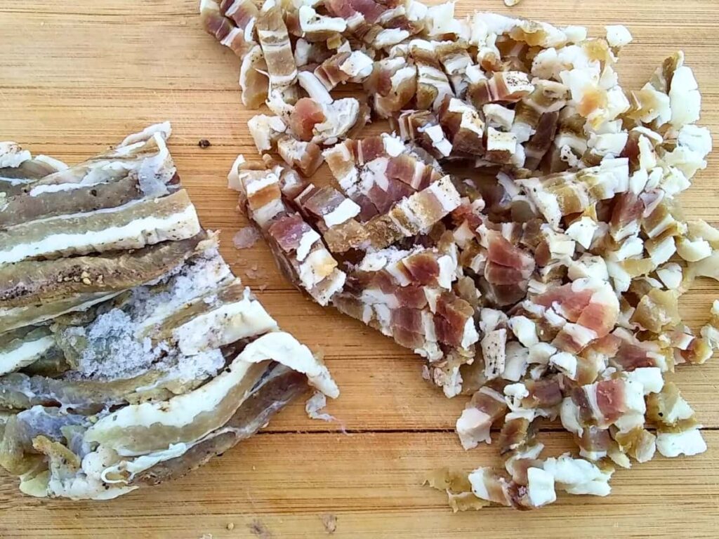 some homemade, home cured bacon on a cutting board with part of it sliced. 
