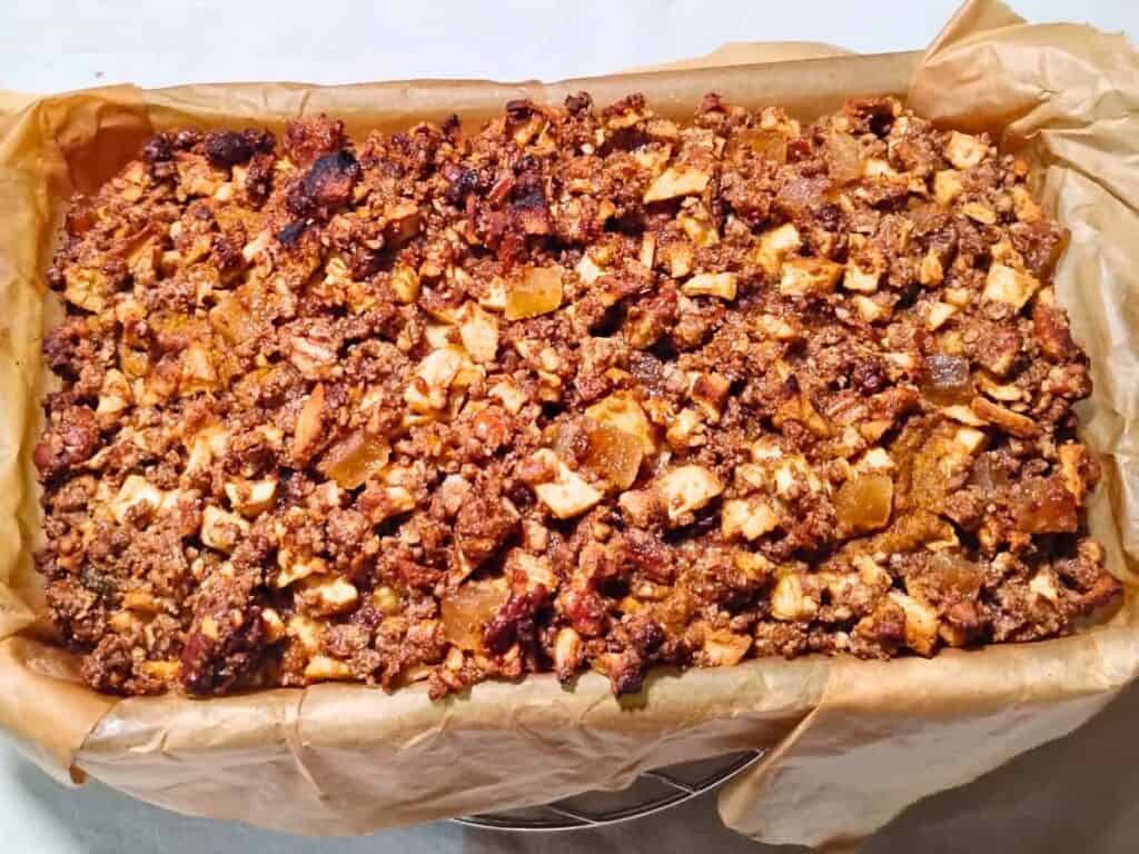 photo of a baked loaf of sourdough pumpkin cake with ginger, pecan & apple streusel inside a parchment lined glass pan.