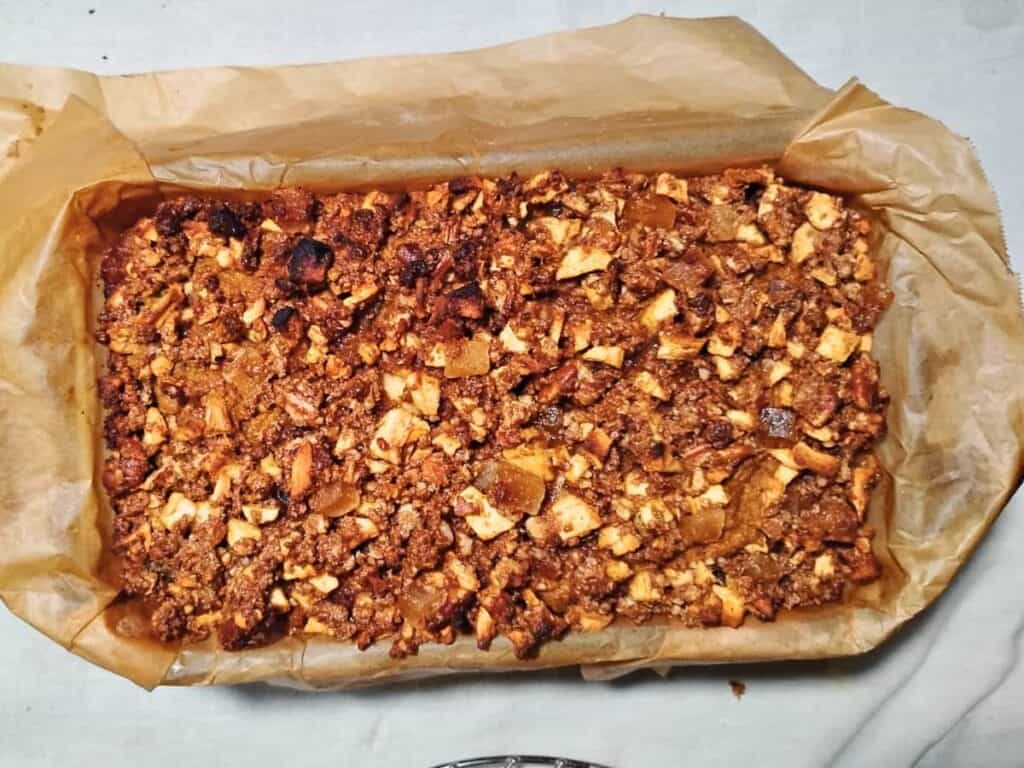 a whole loaf of freshly baked sourdough pumpkin cake with ginger, pecan & apple streusel. in a parchment lined baking pan.