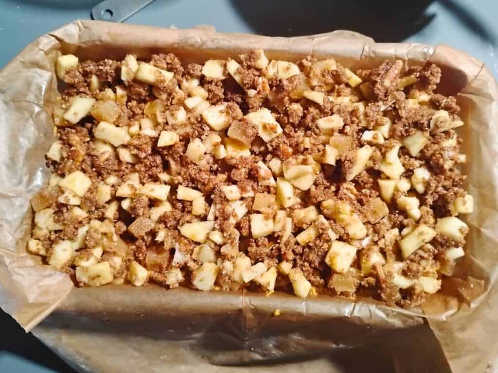 photo of the assembled parts of sourdough pumpkin cake with ginger, pecan & apple streusel in a parchment lined loaf pan, ready for baking. 