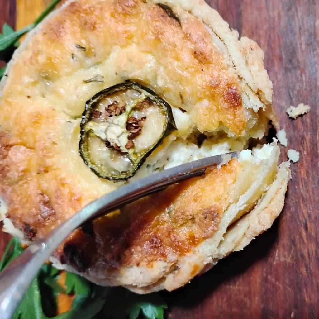 mini quiche in a flaky pie crust with a jalapeno slice on top.