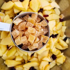 a measuring cup filled with candied diced ginger. A bowl filled with apples and cranberries is sitting below.