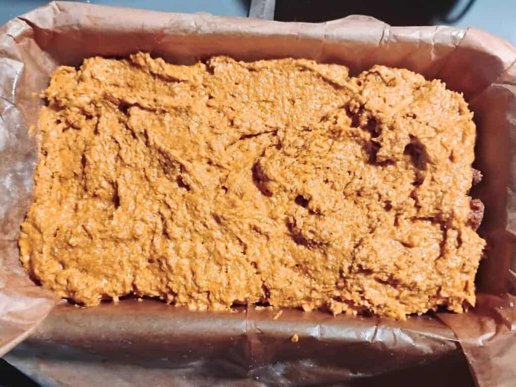 photo shows batter covering the bottom of a parchment lined loaf form.