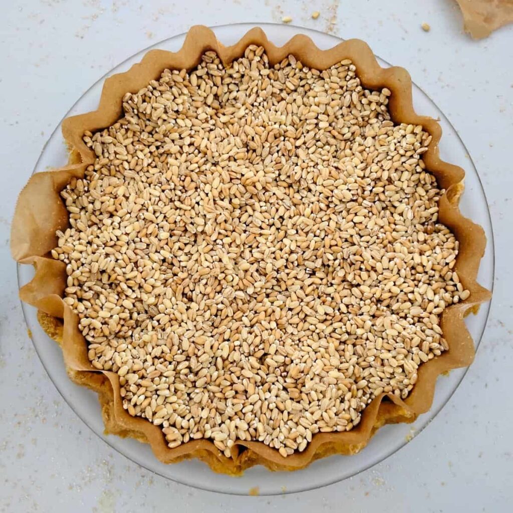 an unbaked crust is lined with parchment paper and filled with barley to blind bake. 
