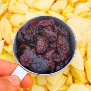 dried cranberries in a measuring cup with peeled, sliced apples below.
