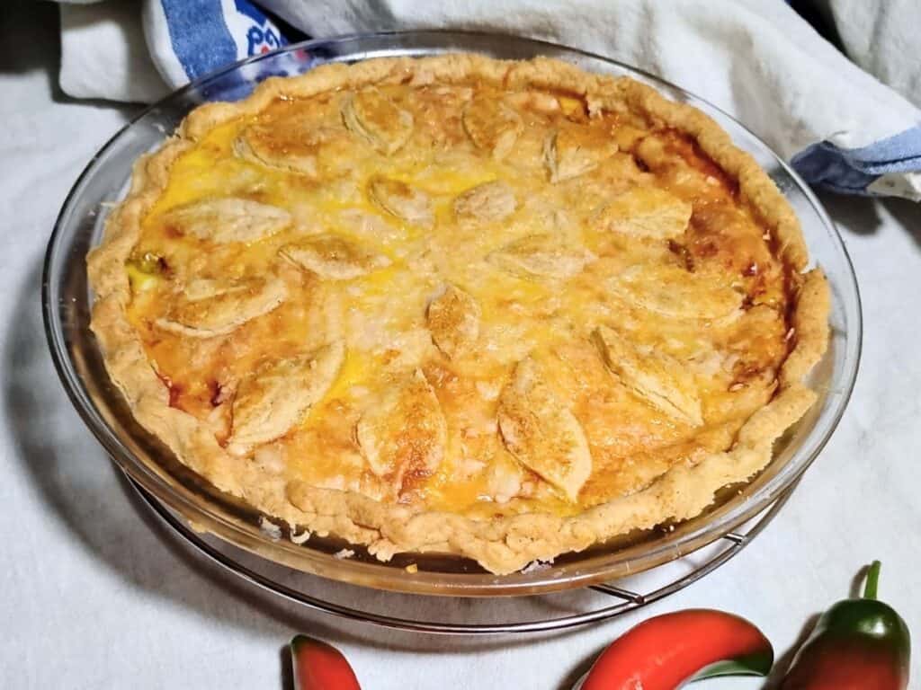 pie plate with a whole baked jalapeno cheese pie in a flaky pie pastry. there are some fresh jalapenos next to it. 