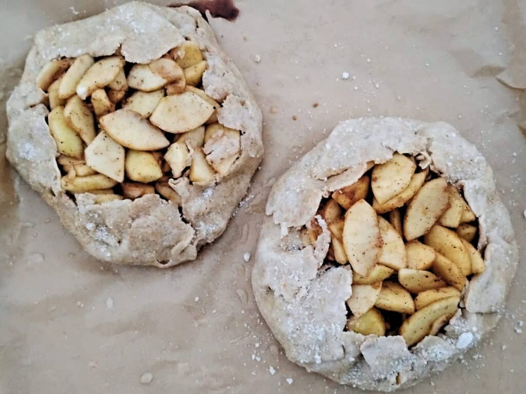 two rustic apple galettes on a sheet.