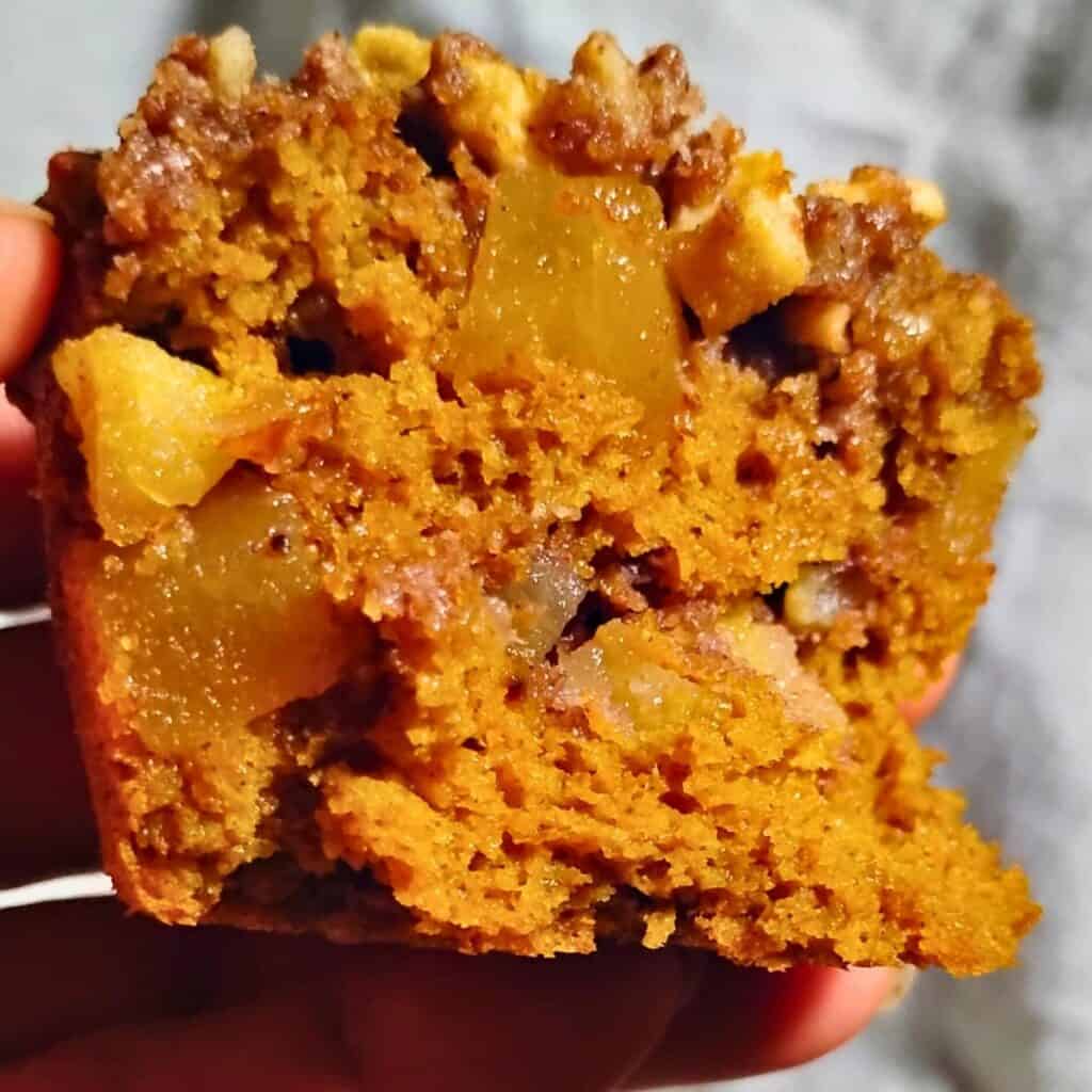 close-up photo of a chunk of sourdough pumpkin cake with ginger, pecan & apple streusel in a person's hand. 