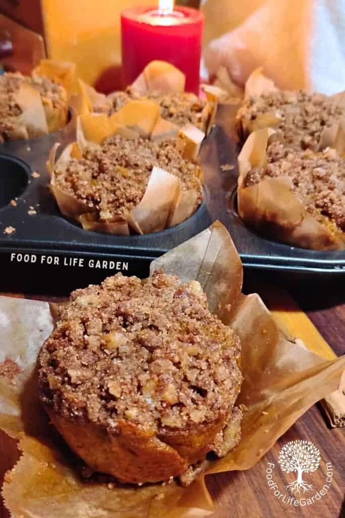 photo of muffins in liners inside a muffin pan with a candle behind it and a muffin in an opened liner in front.