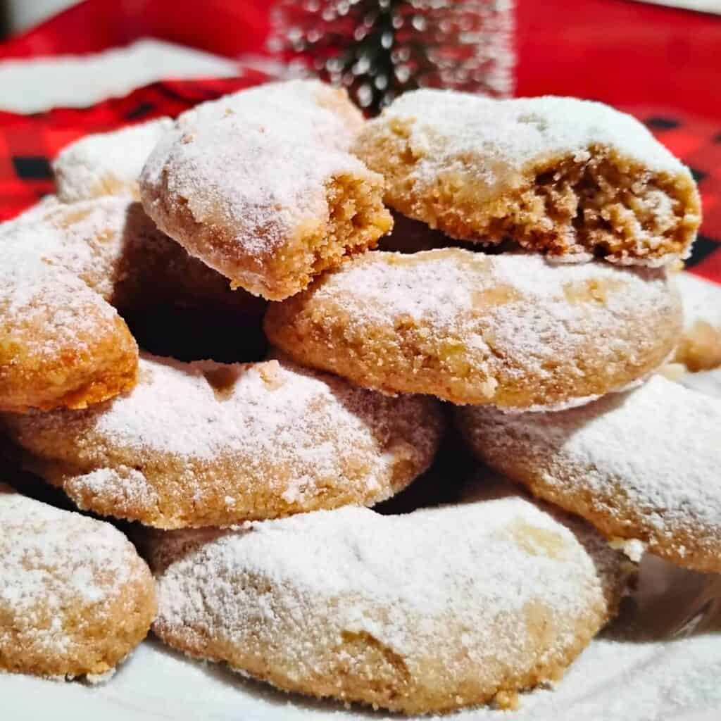 a plate with vanillekipferl piled high and one at the top is broken to show the texture. there is a christmas background.