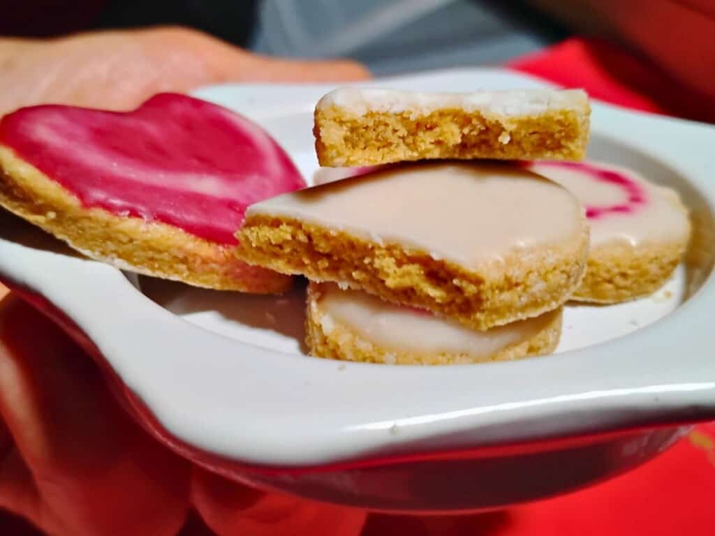a hand is holding a plate with a few zitronenherzen or lemon heart cookies there is one broken on top to reveal the interior. 