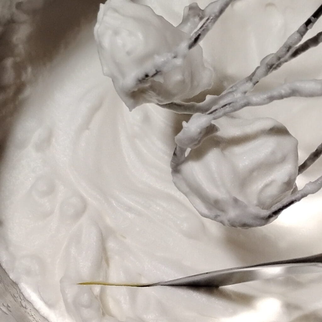 egg whites beaten stiff. in a bowl with a knife cutting into it.