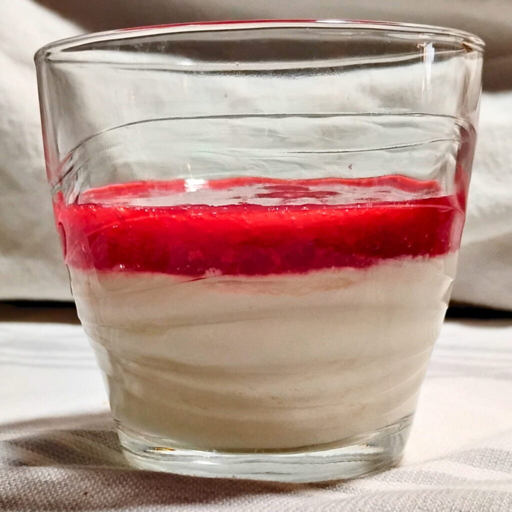 Panna cotta in a glass with a raspberry layer for spooning out.