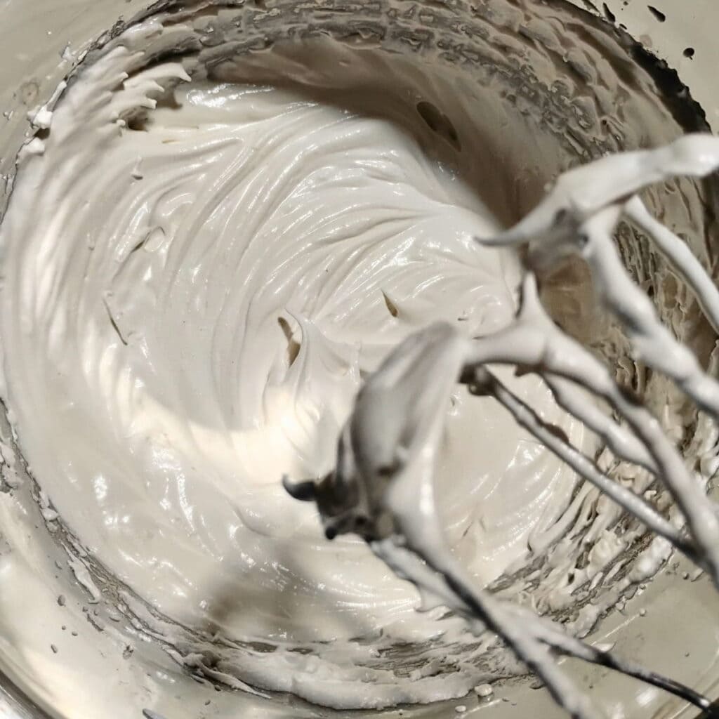 Meringue cream in a bowl with beaters full of the fluff.